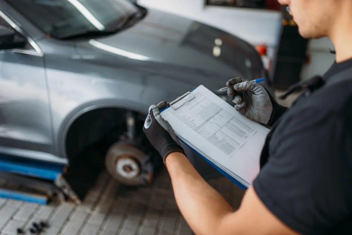 Estimator working through a written claim documentation checklist on a vehicle in a collision repair shop